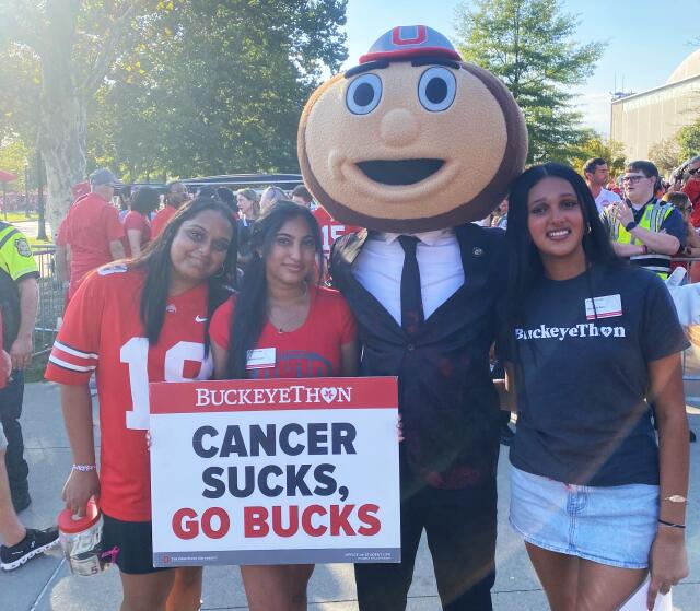 Three students with Brutus Buckeye holding a sign that says "Cancer Sucks, Go Bucks!"