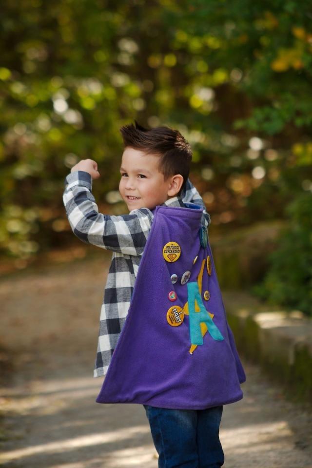 A young boy wearing a purple superhero cape