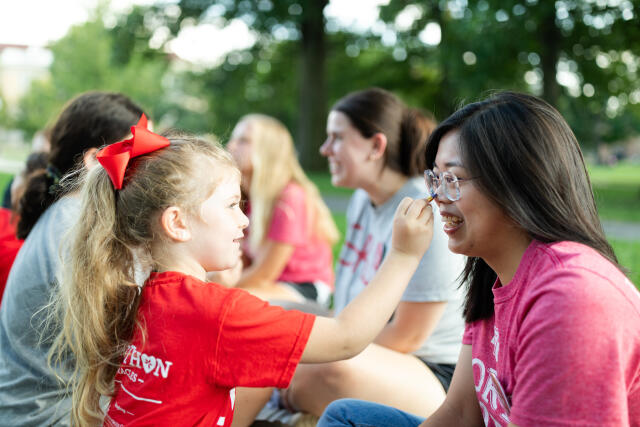 A young girl puts facepaint on a team captain while others hang out in the background.