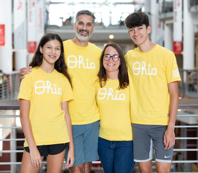 The Varughese family wearing yellow script Ohio shirts inside the Ohio Union
